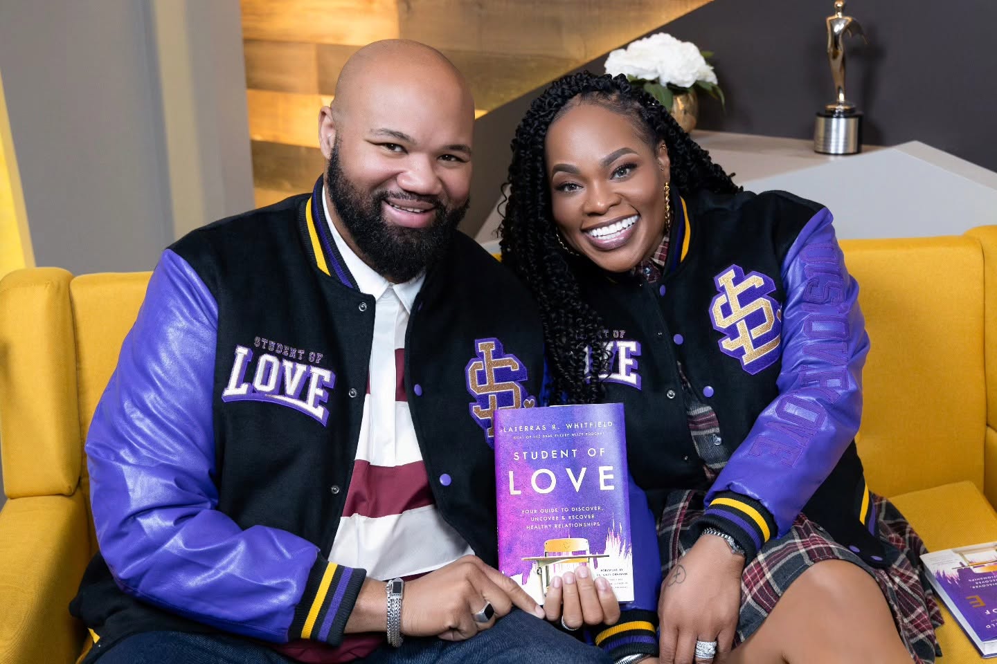 A couple wearing Student of Love jackets and holding the book