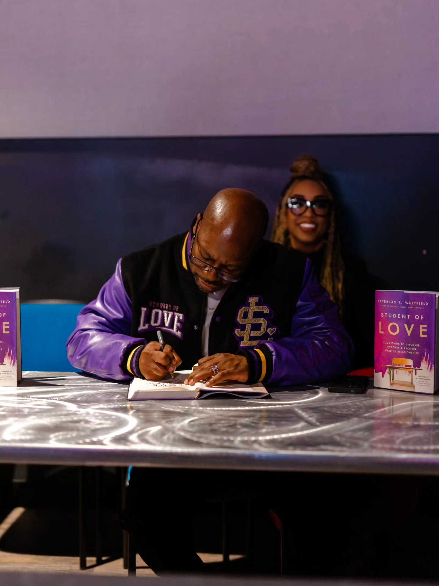 Laterras signing a Student of Love book while wearing the varsity jacket
